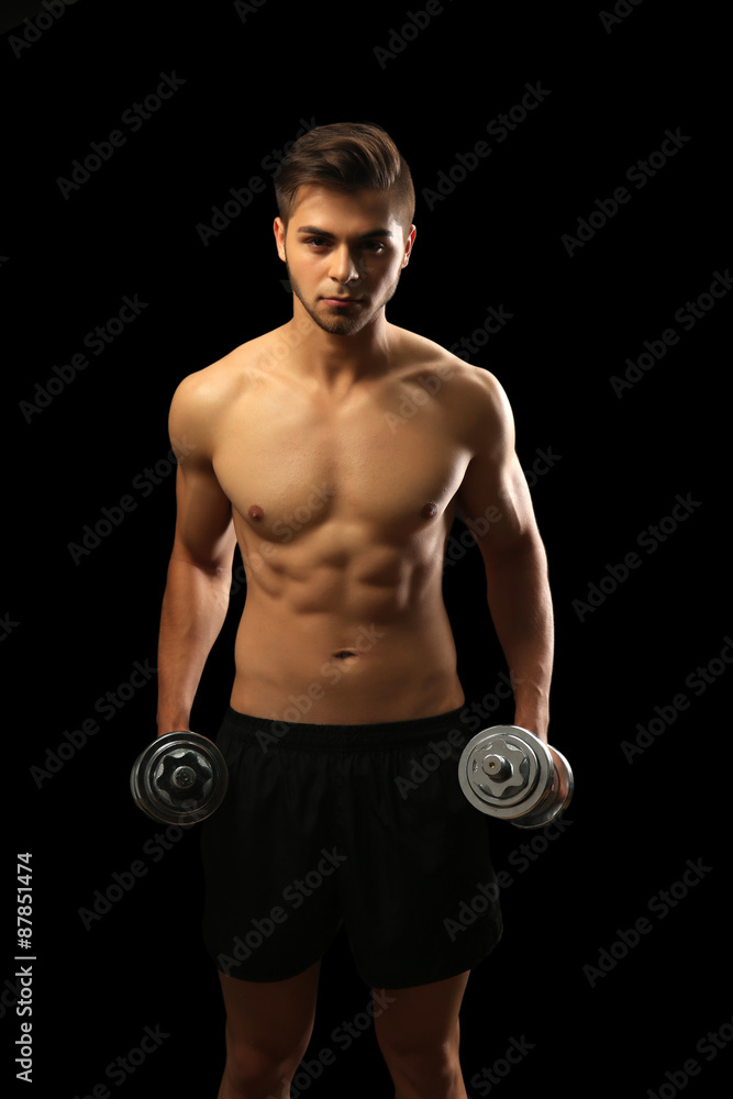 Muscle young man holding dumbbells on dark background Muscle young man holding dumbbells on dark background