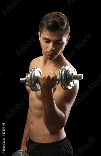 Fototapeta Naklejka Na Ścianę i Meble -  Muscle young man holding dumbbell on dark background