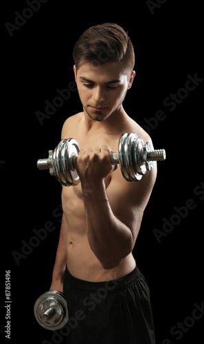 Muscle young man holding dumbbells on dark background