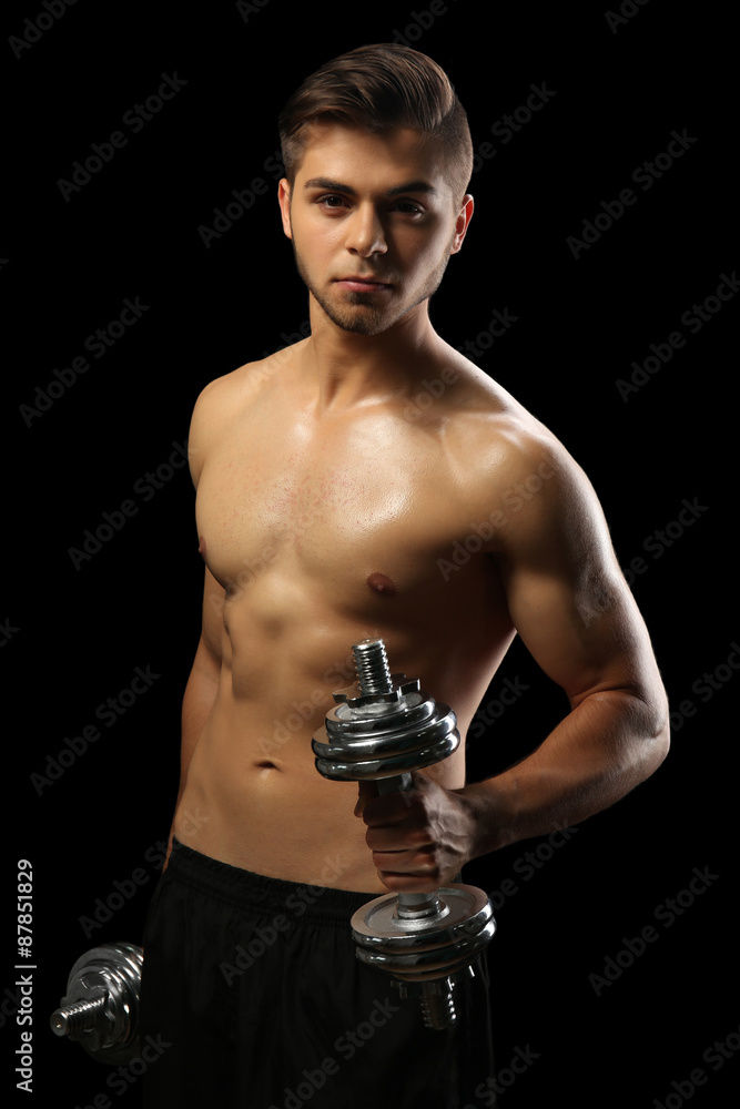 Muscle young man holding dumbbells on dark background Muscle young man holding dumbbells on dark background