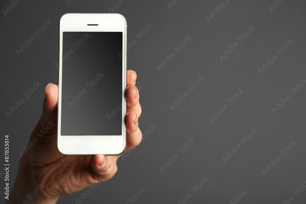 Hand holding mobile smart phone on gray background Hand holding mobile smart phone on gray background