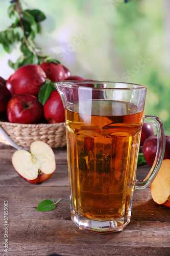 Full jug of apple juice and fruits on bright background