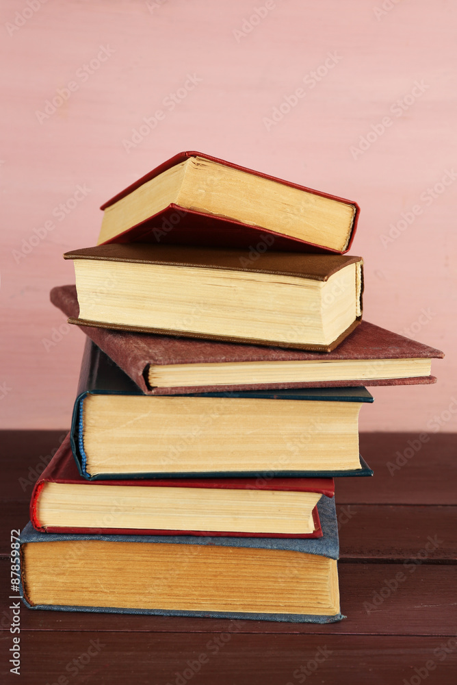 Stack of books on wooden table on pink wall background Stack of books on wooden table on pink wall background