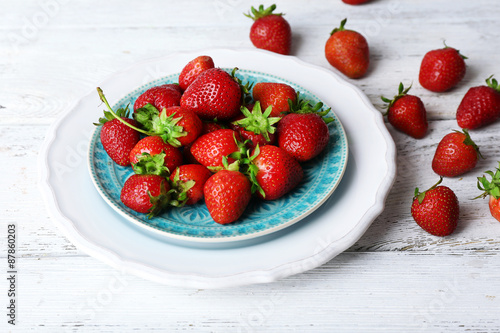 Ripe strawberries in plate on wooden background