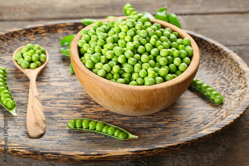 Fresh green peas in bowl on wooden tray, closeup