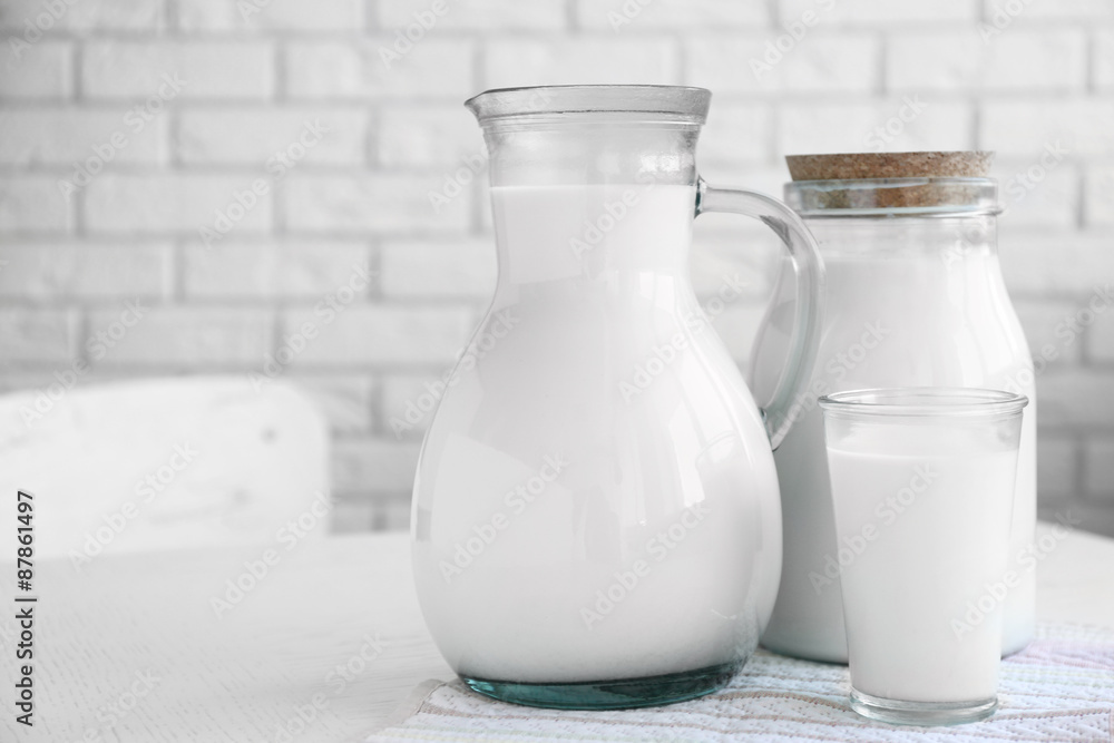 Pitcher, jar and glass of milk on wooden table, on bricks wall background Pitcher, jar and glass of milk on wooden table, on bricks wall background