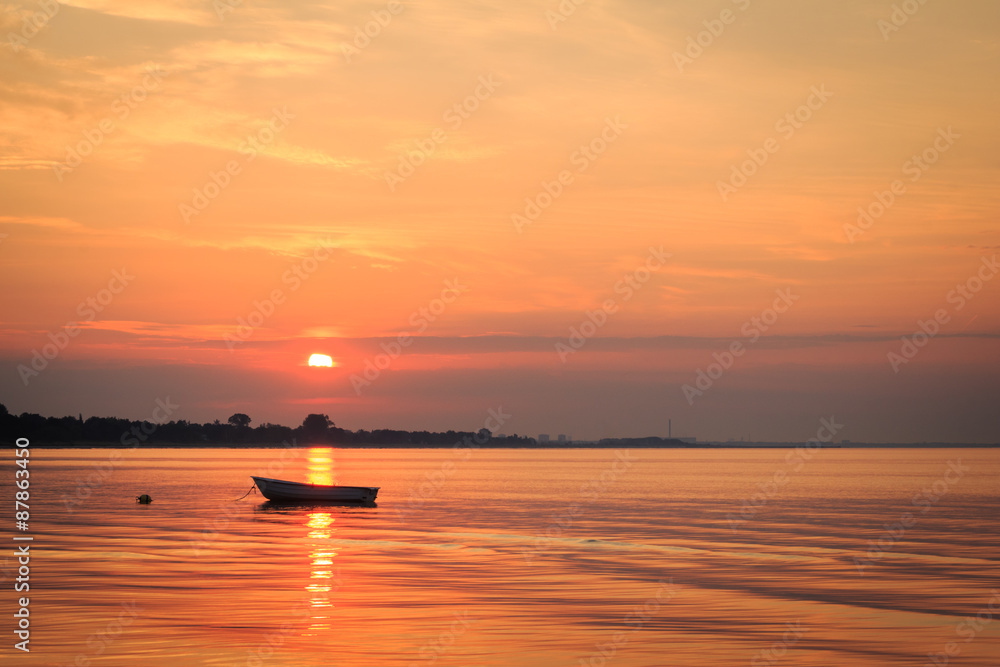Fototapeta premium Boat in the ocean with the sun rising behind it