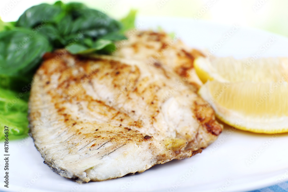 Dish of fish fillet with greens and lemon on plate close up Dish of fish fillet with greens and lemon on plate close up