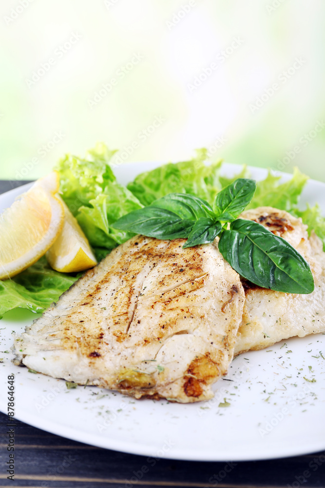 Dish of fish fillet with greens and lemon on bright background Dish of fish fillet with greens and lemon on bright background