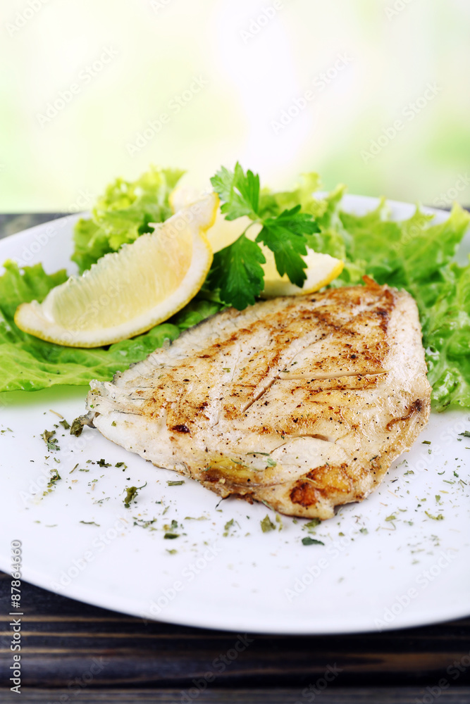 Dish of fish fillet with greens and lemon on bright background Dish of fish fillet with greens and lemon on bright background
