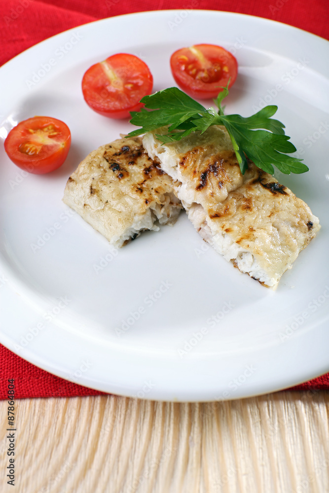 Dish of fish fillet with parsley and tomato on plate close up