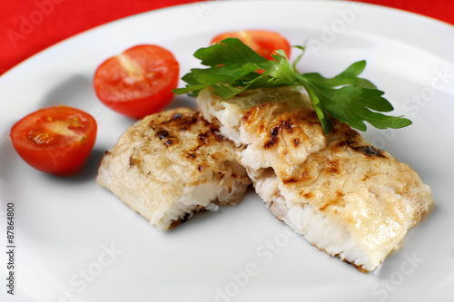 Dish of fish fillet with parsley and tomato on plate close up