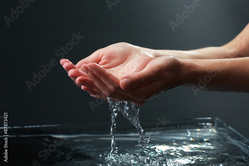 Female hands with water splashing on dark background