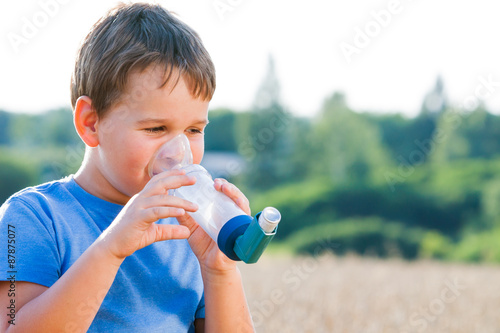 Boy using inhaler for asthma in village with summer sunset