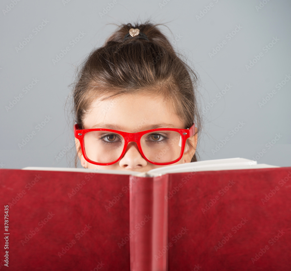 Serious girl in red-framed glasses looking over the book Serious girl in red-framed glasses looking over the book
