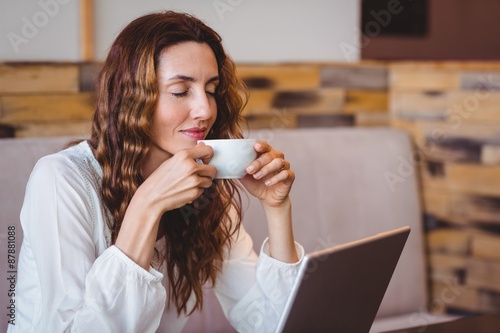 Vászonkép Pretty brunette having coffee using laptop