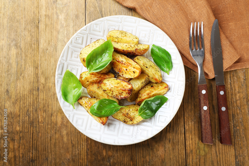 Baked potatoes with basil leaves in white plate on wooden table, top view