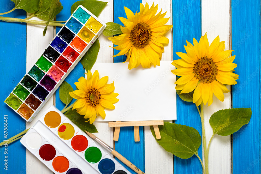 Fototapeta premium sunflowers, painting and easel on the background of colored wooden boards
