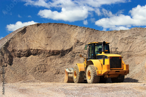 Bulldozer in sand and gravel site with cloudy blue sky