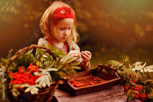 happy child girl making rowan berry beads in sunny autumn garden