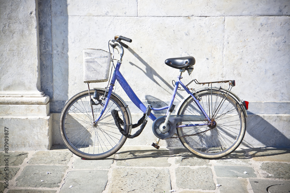 Old blue women bicycle with basket against a marble wall