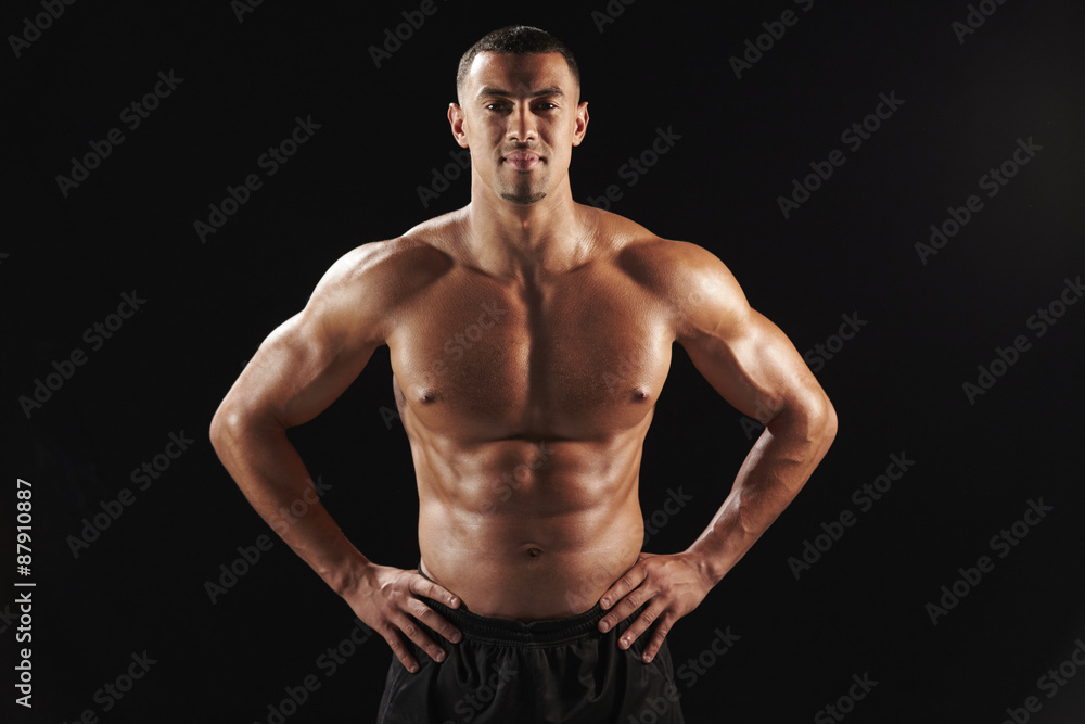 Smiling bare chested male body builder with hands on hips