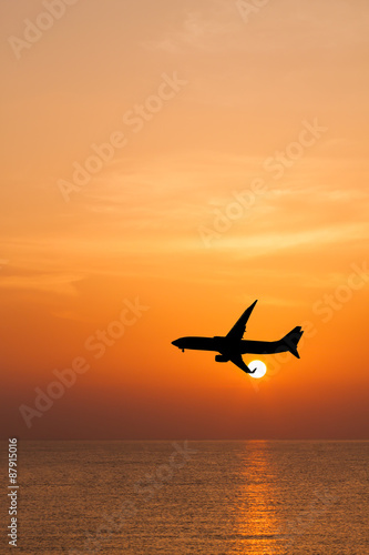 Silhouetted commercial airplane flying above the sea at sunset