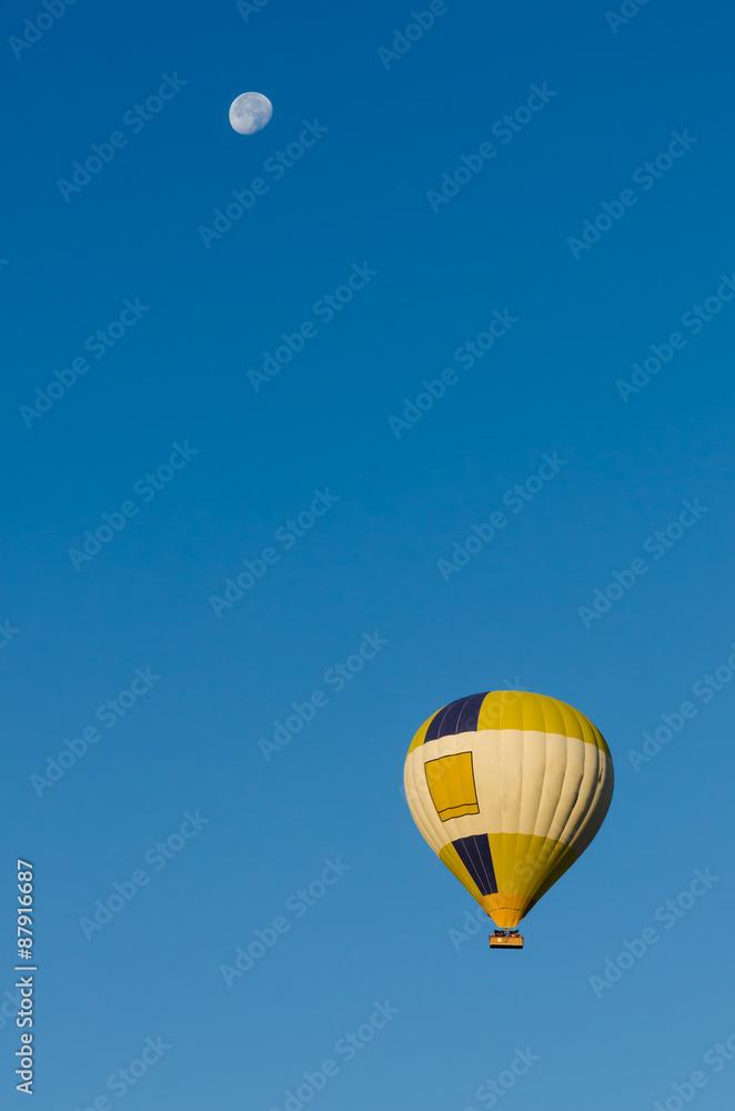 Fototapeta premium Hot Air Balloon flying over clear blue sky with Moon