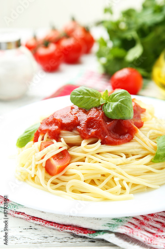 Spaghetti with tomatoes and basil on plate on white wooden backg