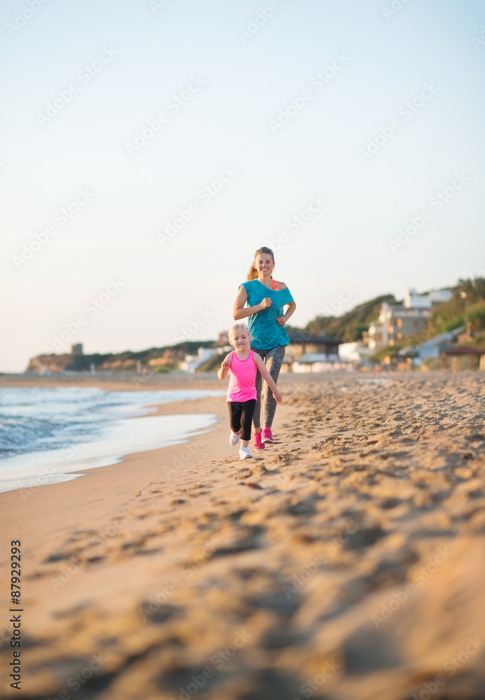 Young mother running behind daughter on the beach at sunset Young mother running behind daughter on the beach at sunset