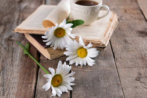 Old book with beautiful flowers and cup of tea on wooden table close up