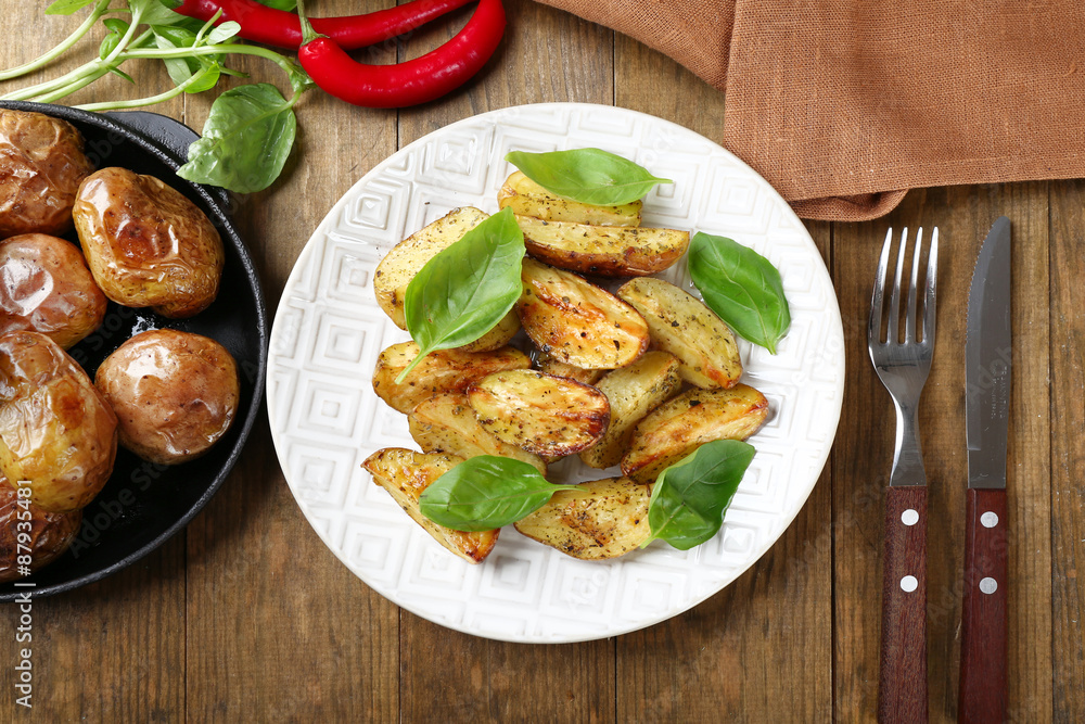 Baked potatoes with basil leaves in white plate on wooden table, top view Baked potatoes with basil leaves in white plate on wooden table, top view