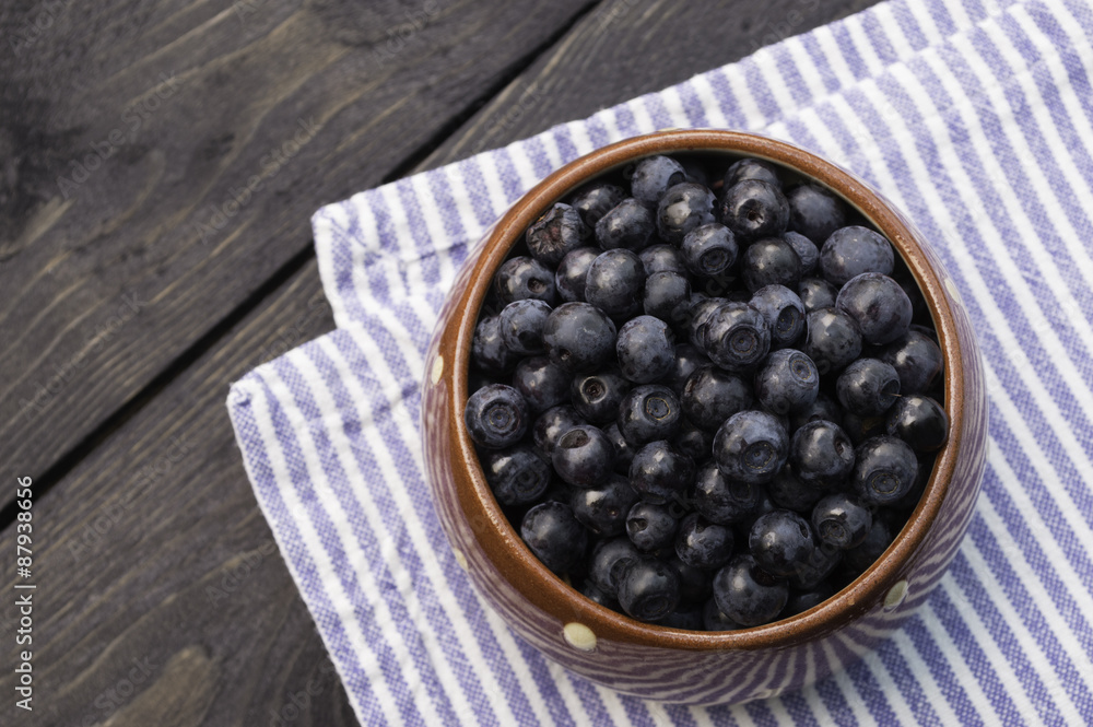Brown dotted ceramic bowl filled with bilberries, rustic style. Wooden table striped blue white towel background, homely. Vertical. Brown dotted ceramic bowl filled with bilberries, rustic style. Wooden table striped blue white towel background, homely. Vertical.