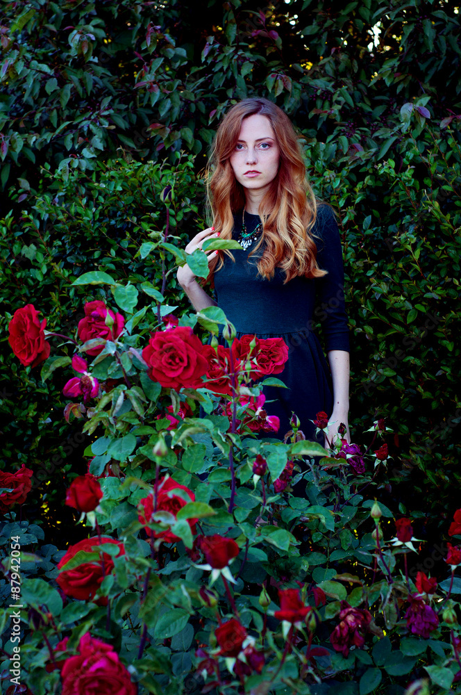 Young woman with auburn hair sitting in the rose garden