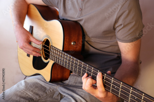 Young man playing on acoustic guitar close up
