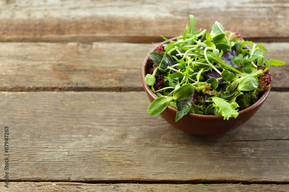 Fototapeta premium Fresh mixed green salad in bowl on wooden table close up