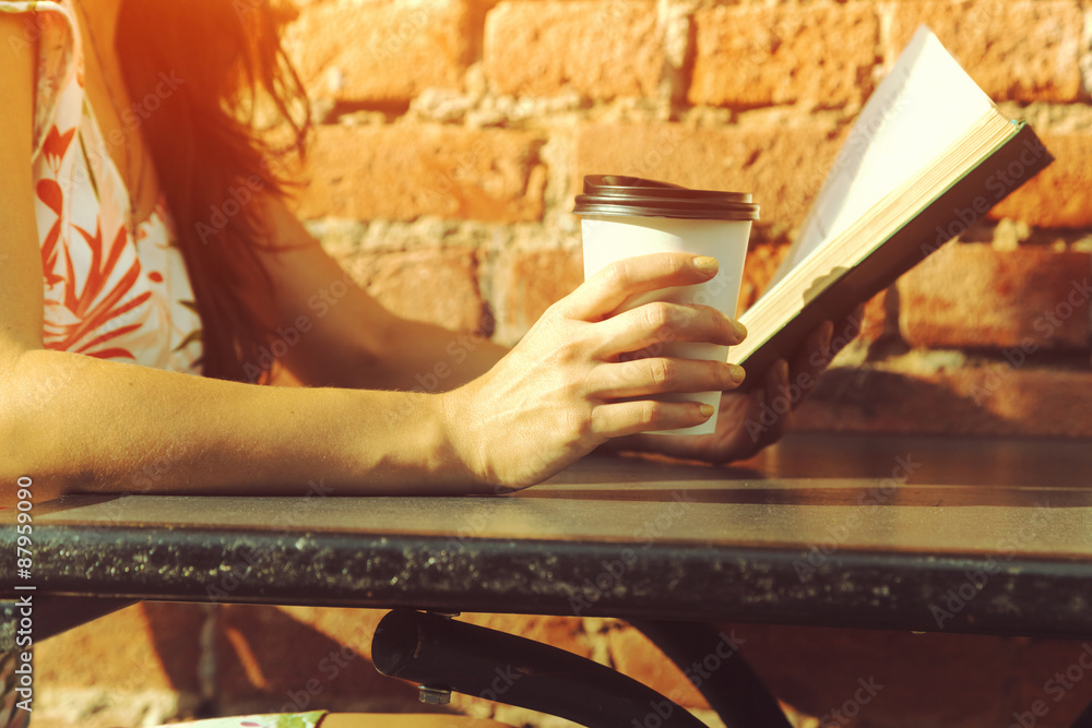 girls hands holding morning coffee and book at cafe table