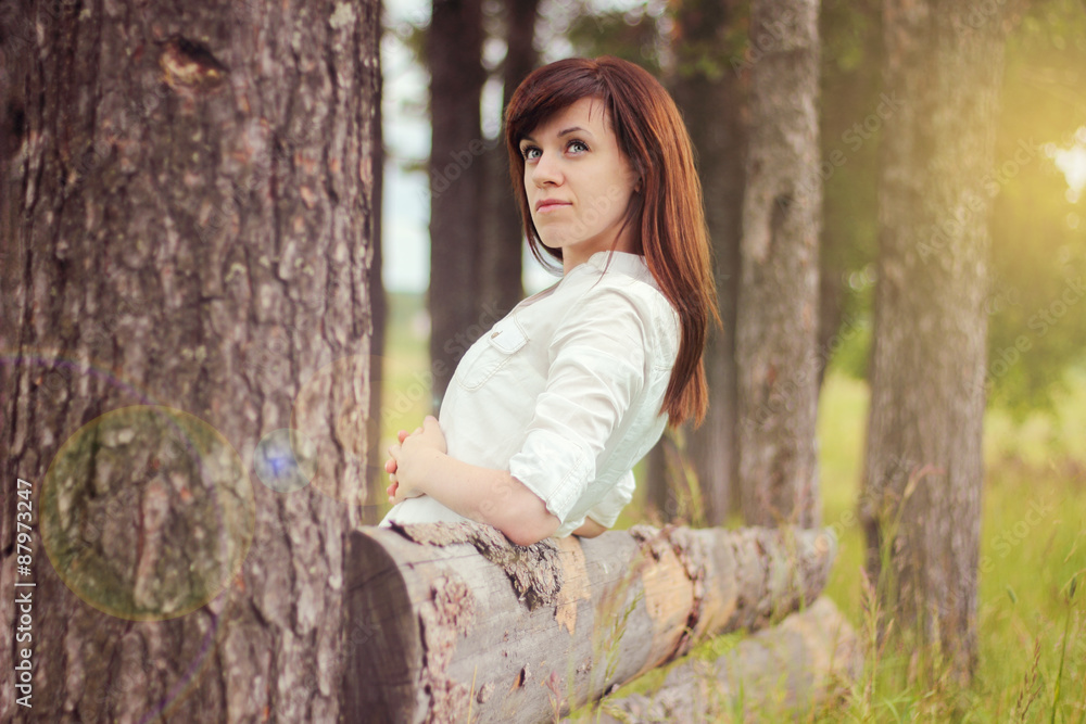 Beautiful girl in a white shirt looks out from behind a tree, the sun Beautiful girl in a white shirt looks out from behind a tree, the sun