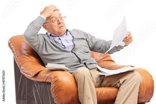 Shocked senior man looking at his bills in disbelief
