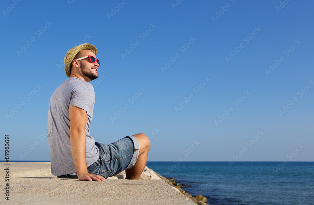 Happy man sitting by the sea with hat