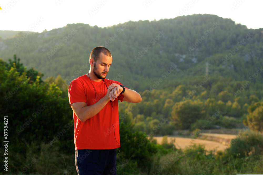 Fototapeta premium Healthy sports man standing outdoors looking at watch