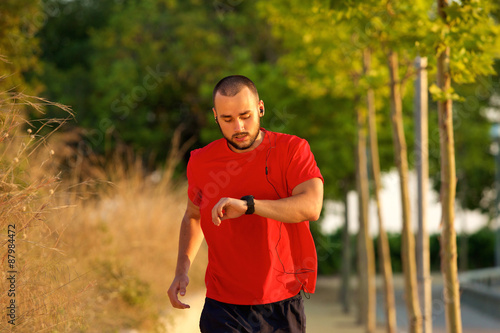 Man running outdoors checking time on watch © mimagephotos