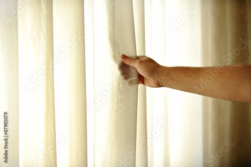 Man's hand pulling a window curtain