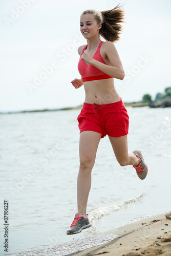 Young lady running at the sunny summer sand beach. Workout. Jog