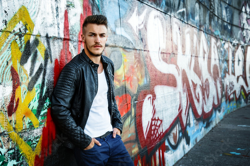 Attractive young man in white shirt and black jacket on graffiti background