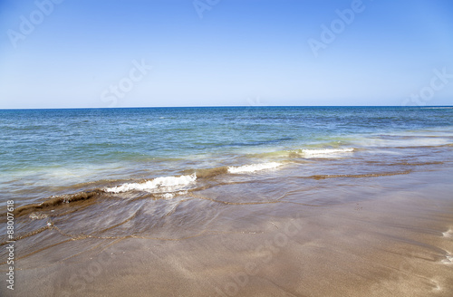 orilla del mar con olas arena y al fondo el horizonte entre el mar y el cielo azul