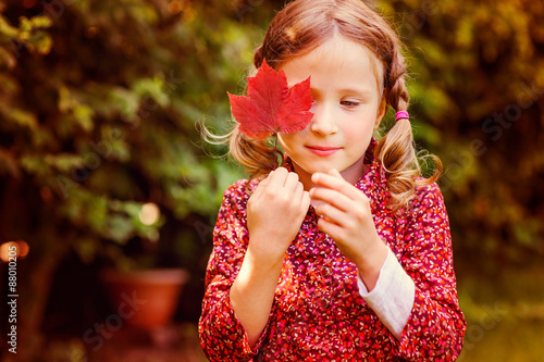 portrait of cute child girl playing with red autumn leaf 