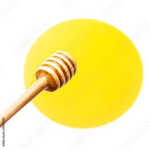 Wooden honey dipper with yellow honey flowing drops isolated on