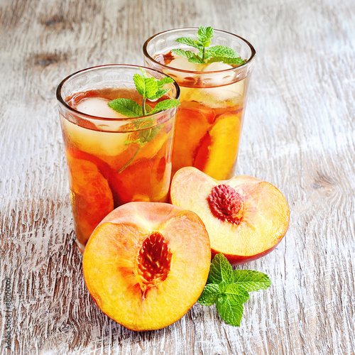Refreshing iced tea with ripe peaches on rustic background, selective focus