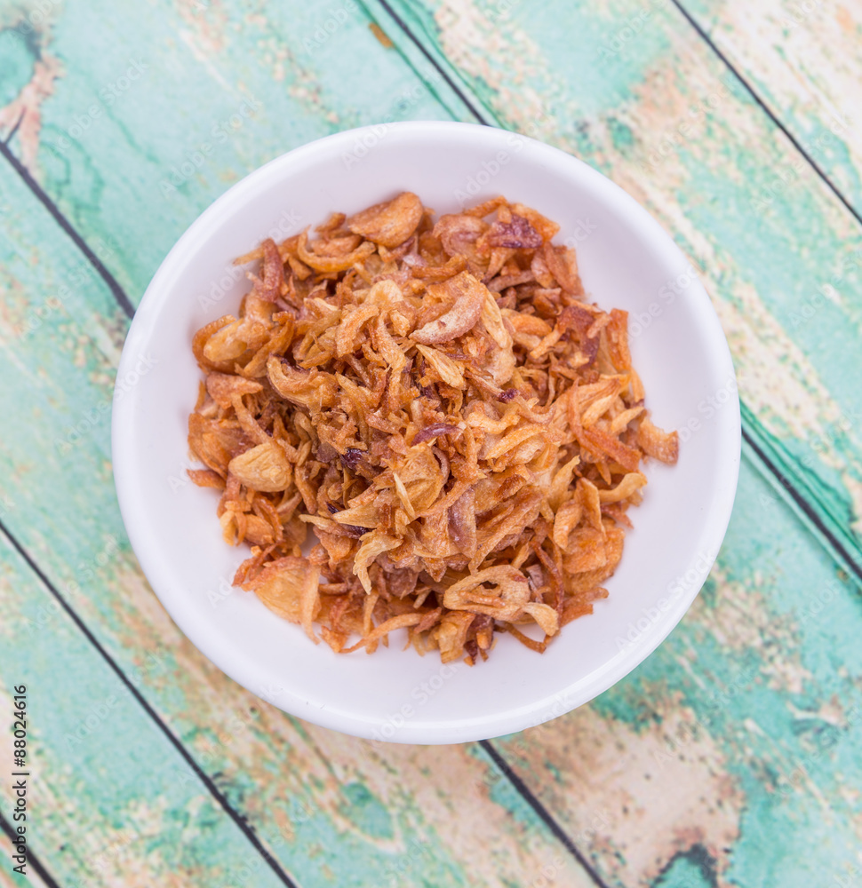 Deep fried shallots for garnishing in white bowl over wooden background Deep fried shallots for garnishing in white bowl over wooden background